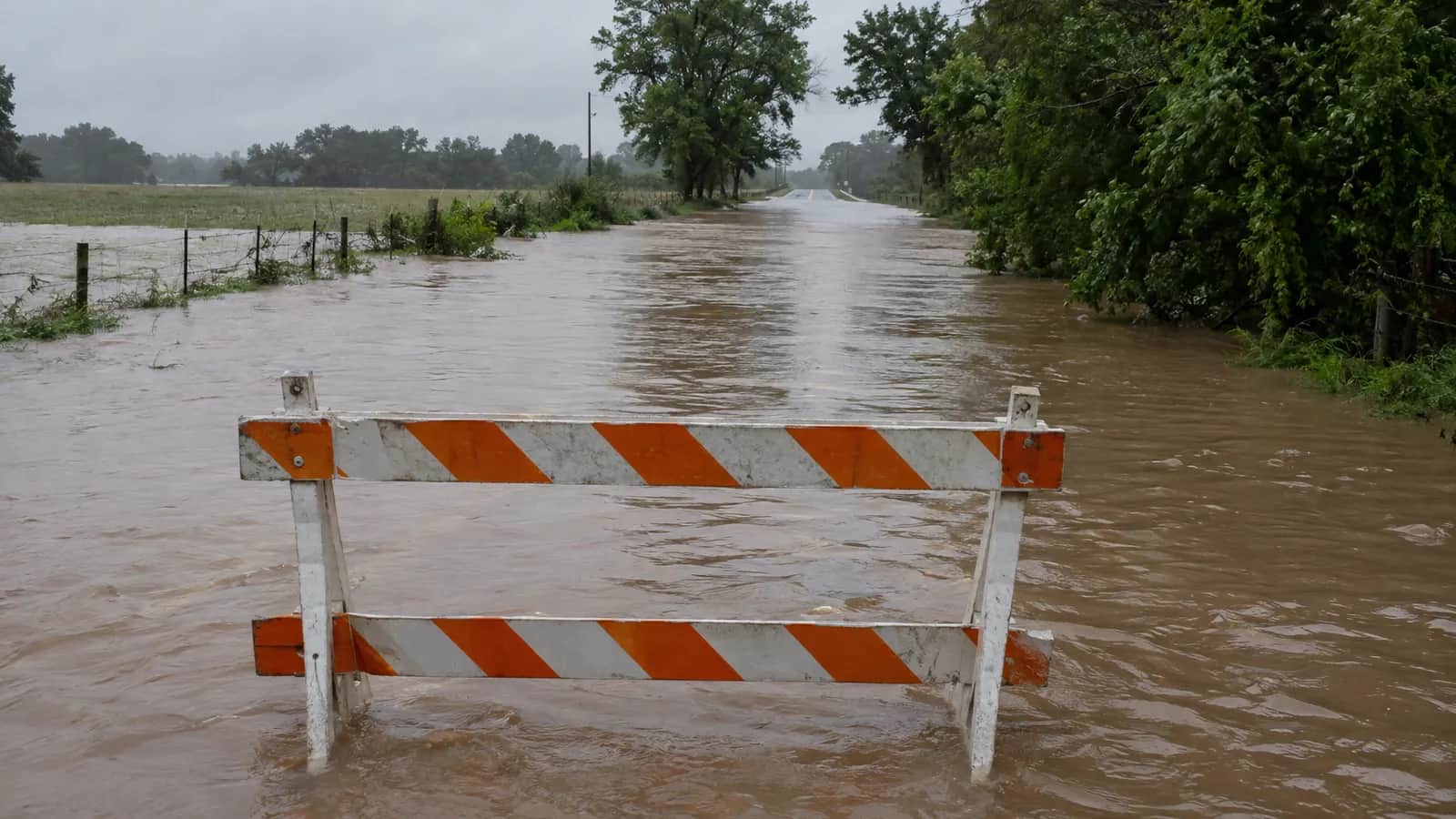 Brown water hides the lane markings behind a barricade on a flooded road.