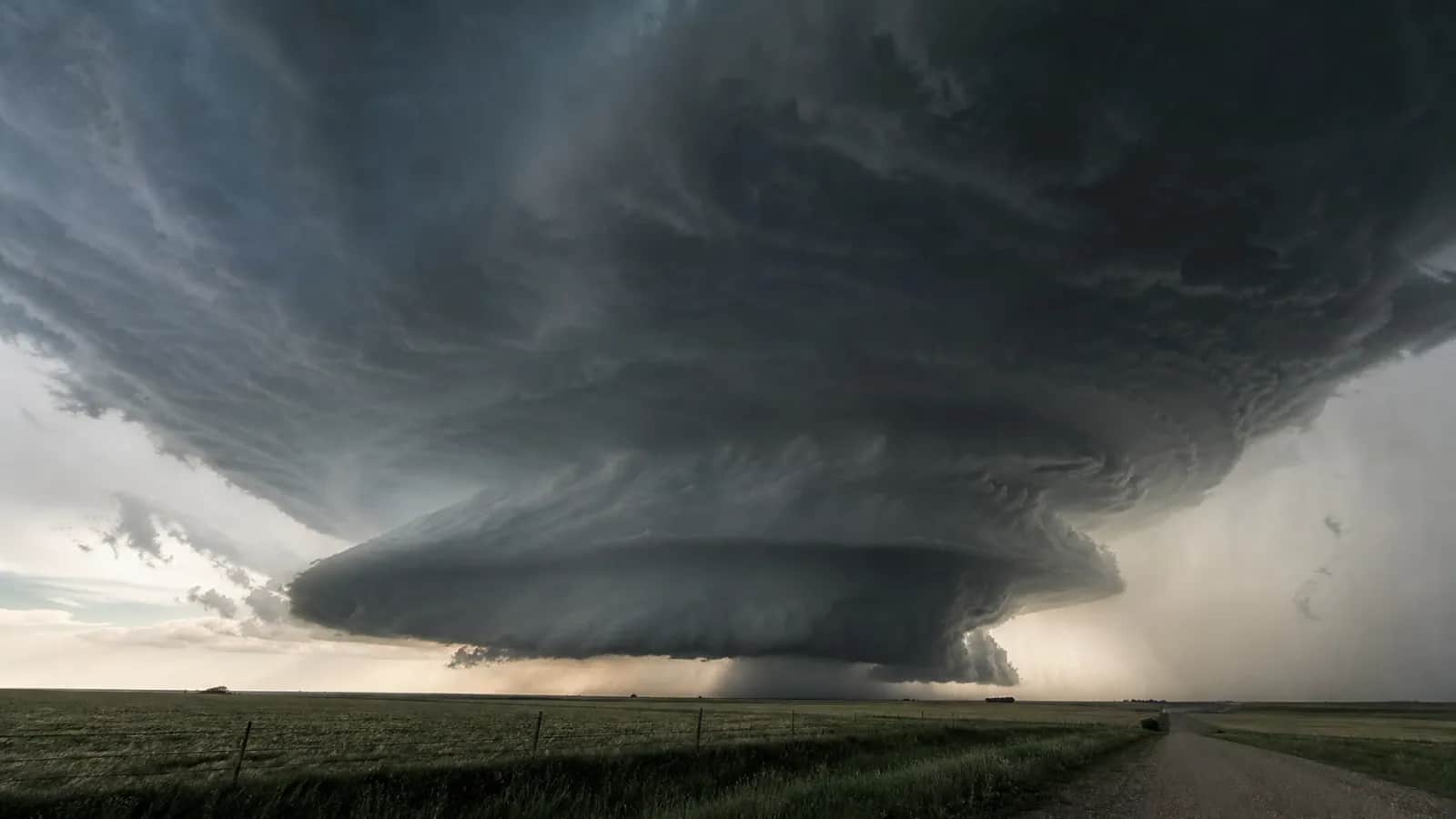 Supercell with stacked cloud base over farmland, dirt road and fence in foreground