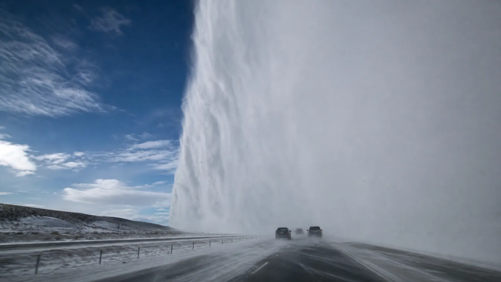 Highway where blue sky meets a wall of snow, three vehicles entering the squall